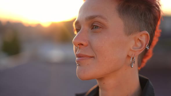 Headshot of Thoughtful Pierced Redhead Caucasian Woman Posing in Sunrays Standing on Roof in Urban alt