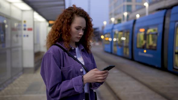 Young woman with smartphone standing on platform waiting for train