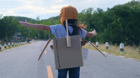 Cute dreamer little girl running on a lakeside road with a cardboard plane on a sunny day. alt
