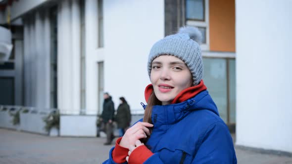 Beautiful Young Girl in a Blue Jacket Portrait Touches Her Hair and Smiles alt