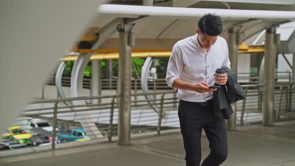 Asian young business man walking up on stair going to work and chat on mobile phone outdoor. alt