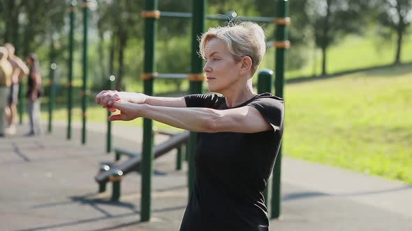 An Elderly Woman Does a Warmup in the Park on the Playground