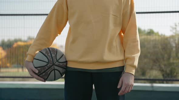 Man Stands on a Basketball Court in the Park Holding a Ball