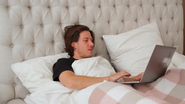 Young Man Lying in the Bed with Laptop Make Morning Stretching and Start Working