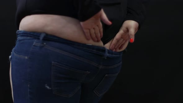 Fat Woman with Cellulite Trying to Put on Jeans on Black Background