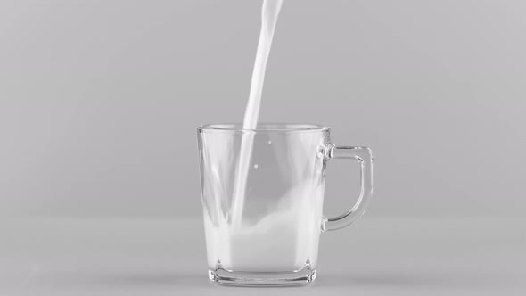 Milk Pouring Into Glass Mug Close Up Isolated on Light Grey Background alt