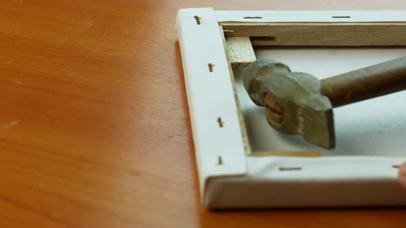 Close-up of the artist stretching the canvas over the frame of the painting. alt