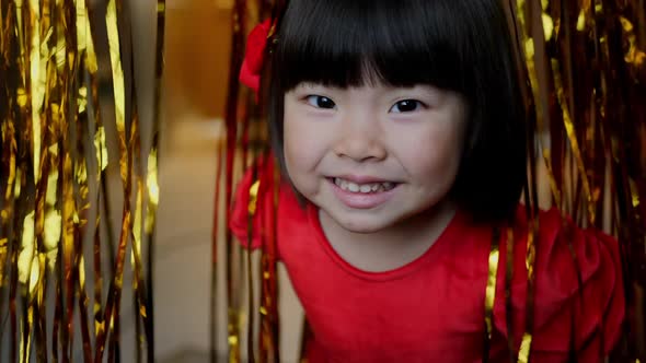 Korean Girl Child in Red Dress is Playing on Christmas Night with Golden Tinsel alt