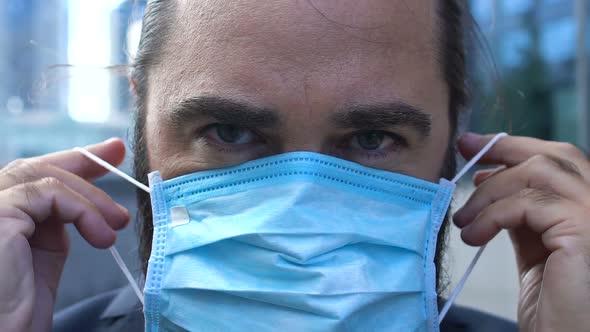 Serious Man Putting on Medical Facemask Close-Up, Big City Air Pollution Concept