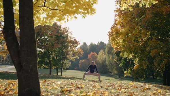 Young Woman Practices Prasarita Padottanasana in Autumn City Park on a Yoga Mat