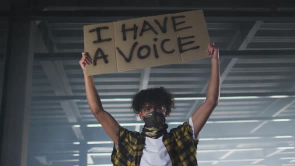 Mixed race man wearing face mask holding protest placard in empty parking garage alt