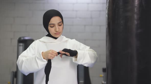 Strong Muslim Woman Prepares for Training Boxing Alone in the Gym Woman Ties Ricky Elastic Bandages alt