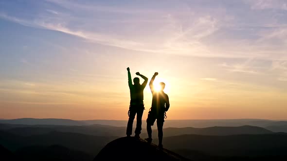 Silhouettes of a Happy Young Couple on Top of a Mountain Triumphantly Raising Their Hands in the Air