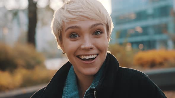 Portrait of Young Caucasian Woman with Short Blond Hair Winking in the City Park alt
