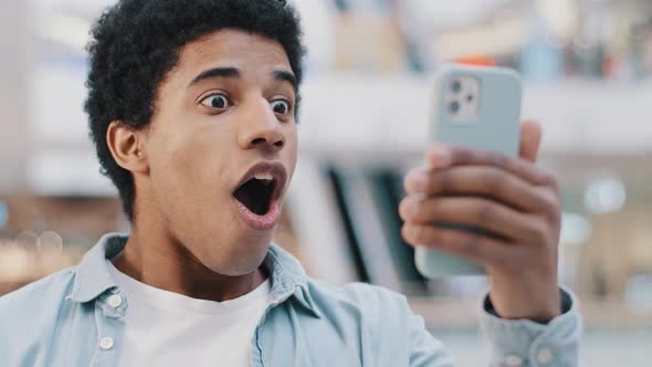 African American Surprised Shocked Amazed Man User Guy Teenager Looking at Mobile Phone Opens Mouth alt