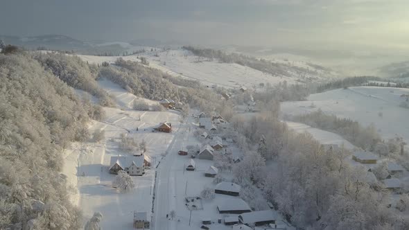 Mountain Village in the Snow From a Height. Flight Over a Village in Carpathian Mountains in Winter alt