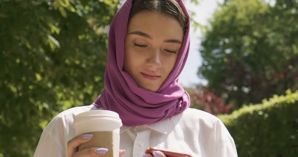Beautiful Young Woman Drink Coffee and Looking at Smartphone, Wearing Traditional Headscarf alt