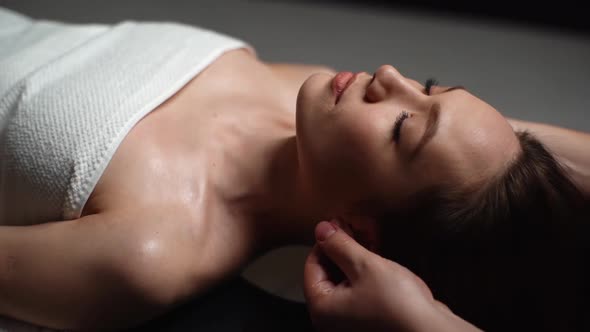 Closeup of Male Masseur Massaging Auricle of Young Woman Lying Down in Massage Table at Spa Salon alt