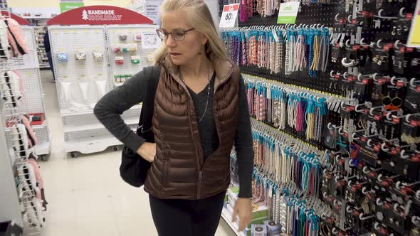 Pretty blonde, mature woman walking through aisles of beads and earrings in a craft store. alt