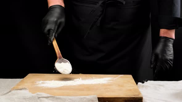 chef in black uniform and black latex gloves holds a wooden spoon with  flour alt