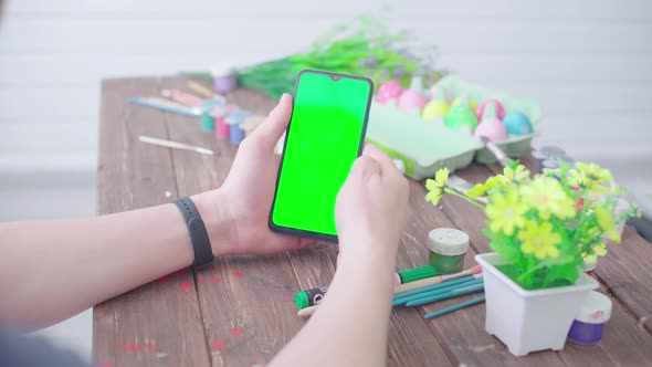 A Man Prepares for Easter Paints Easter Eggs and Uses a Smartphone with Chroma Key alt