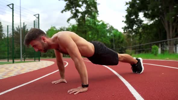 Man in Black Shorts Shirtless Doing Push Ups on Race Track Stadium Outdoors alt