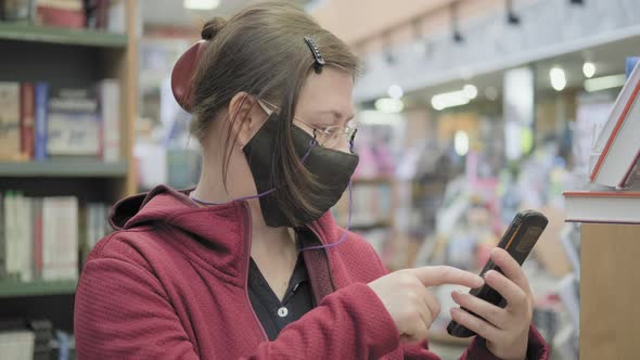 Woman Wearing Glasses and Mask in Bookstore Takes Pictures of Books on Her Phone