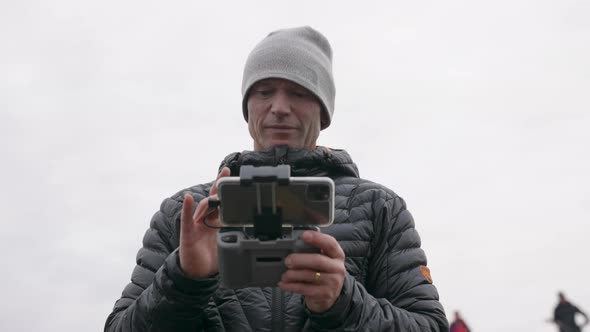 Photographer Using Remote Control Handset To Control Drone alt
