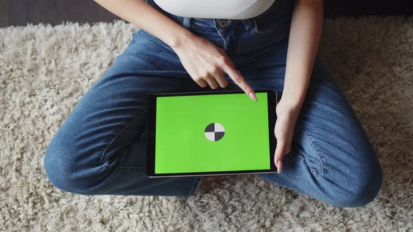 Woman Sits on Floor and Swipe Her Finger Over Chromakey Screen of Tablet Top View alt