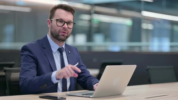 Middle Aged Businessman with Laptop Pointing at the Camera alt