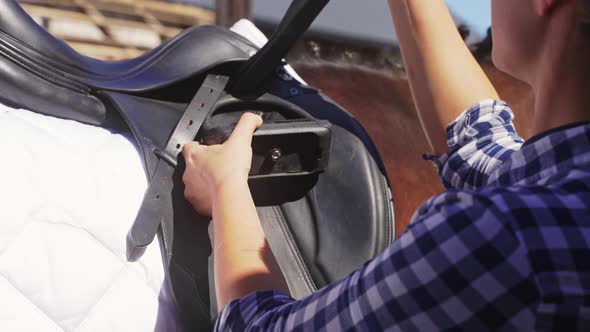 Woman Saddling Up Her Horse For A Competition  Tying Up Leather Strap Of Saddle alt