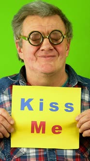 Caucasian Mature Adult Man Smiling and Point Finger at Plaque Lettering Kiss Me alt