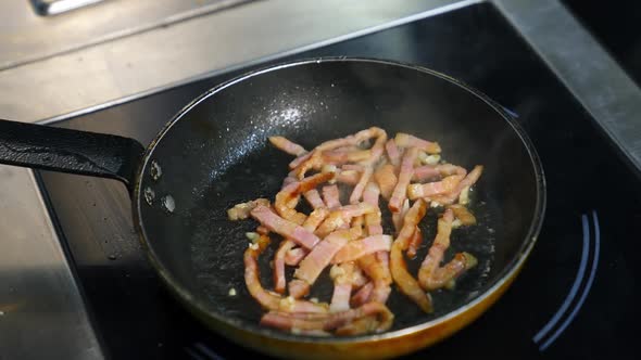 Frying bacon pieces in a pan. Crispy pieces of delicious bacon are fried in a hot skillet. alt