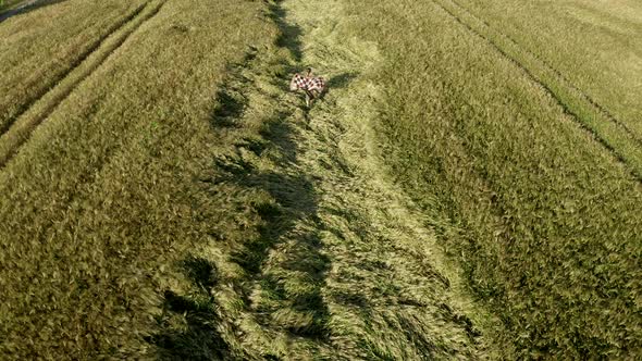 Aerial view young lady running in agricultural wheat field. Shawl fluttering in wind. Harvest Sunset
