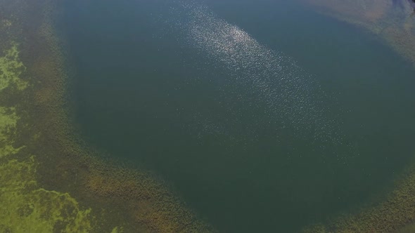 Flying over lake as the sun shimmers on the surface of the water alt