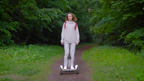 A Girl Dressed in Casual Rides Through the Forest on a Gyro Scooter. Modern Electric Transport. alt