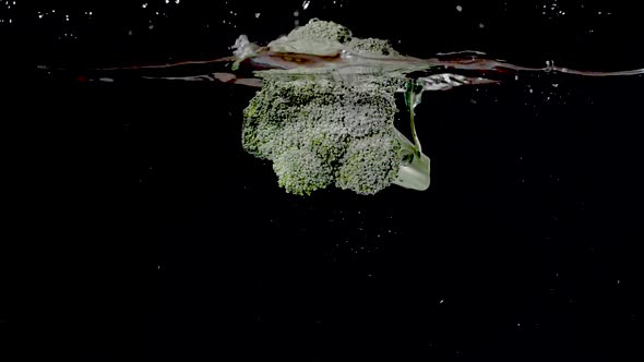 Colorful branch of broccoli being dropped into water in slow motion. alt