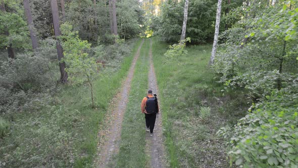 Aerial Drone View Following Young Caucasian Man with Backpack Walking through Forest