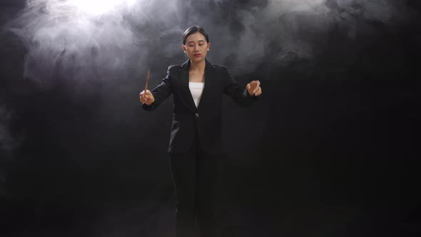 Asian Conductor Woman Holding A Baton Closing Her Eyes And Showing Gesture In The Black Studio alt