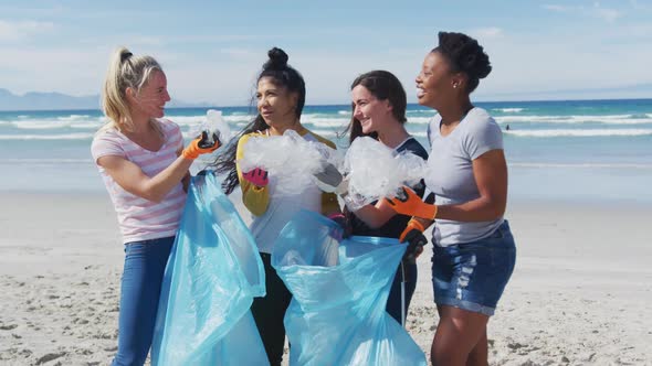 Diverse group of female friends putting rubbish in refuse sacks at the beach alt