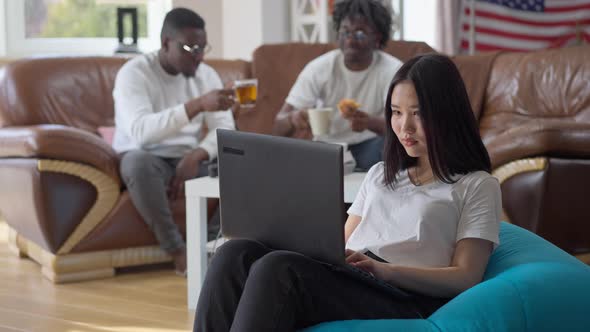 Concentrated Intelligent Asian Woman Typing on Laptop Keyboard As African American Men Talking at alt