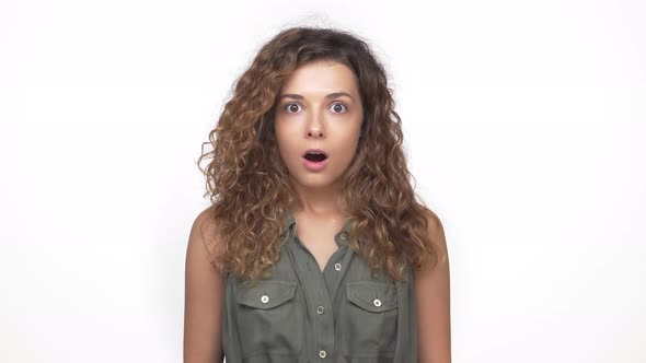 Lady in Grey Shirt with Curly Hair Expressing Worrying Looking Frightened Closing Mouth with Hand alt