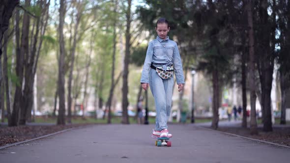 Fashionable Girl Travels Through Park Streets on a Skateboard