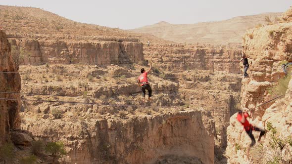 A man balances while tightrope walking and slacklining across a canyon alt