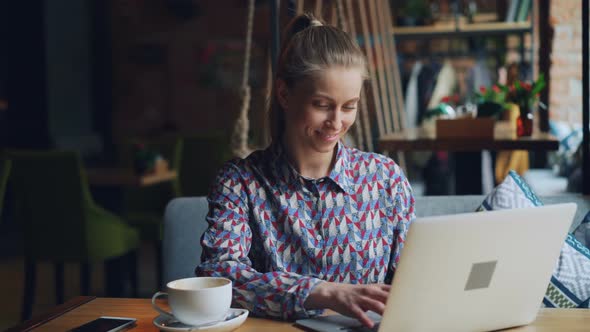 Happy Young Lady Working with Laptop in Cafe Typing Sitting at Table Alone alt