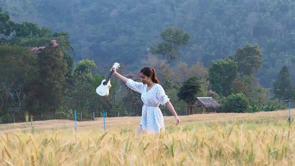 Thai woman who is very beautiful holding her ukulele walking in a barley field.
