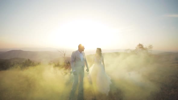 Bride and Groom Hold Their Hand and Walk in Color Smoke in the Autumn Mountains. Front Wide View