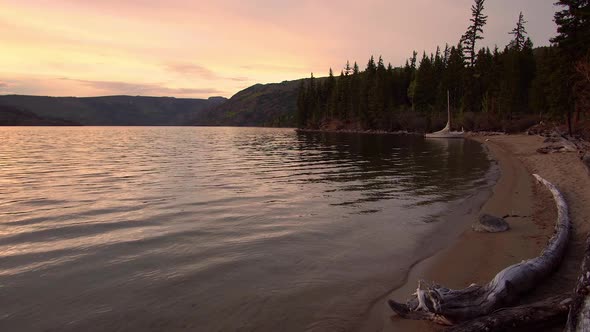 Colorful sunset reflecting in lake viewing shoreline with sailboat alt