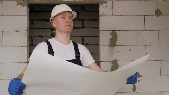 A Male Builder Studies the Drawings Before Starting Repair and Construction Work alt