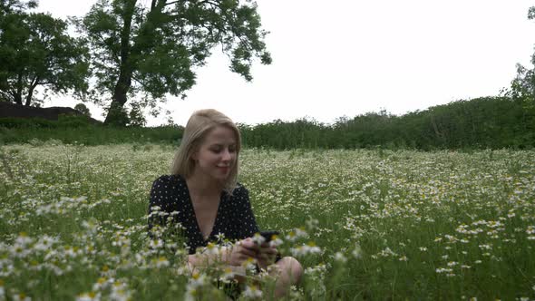 Blonde girl in dark dress in a chamomiles flowers meadow